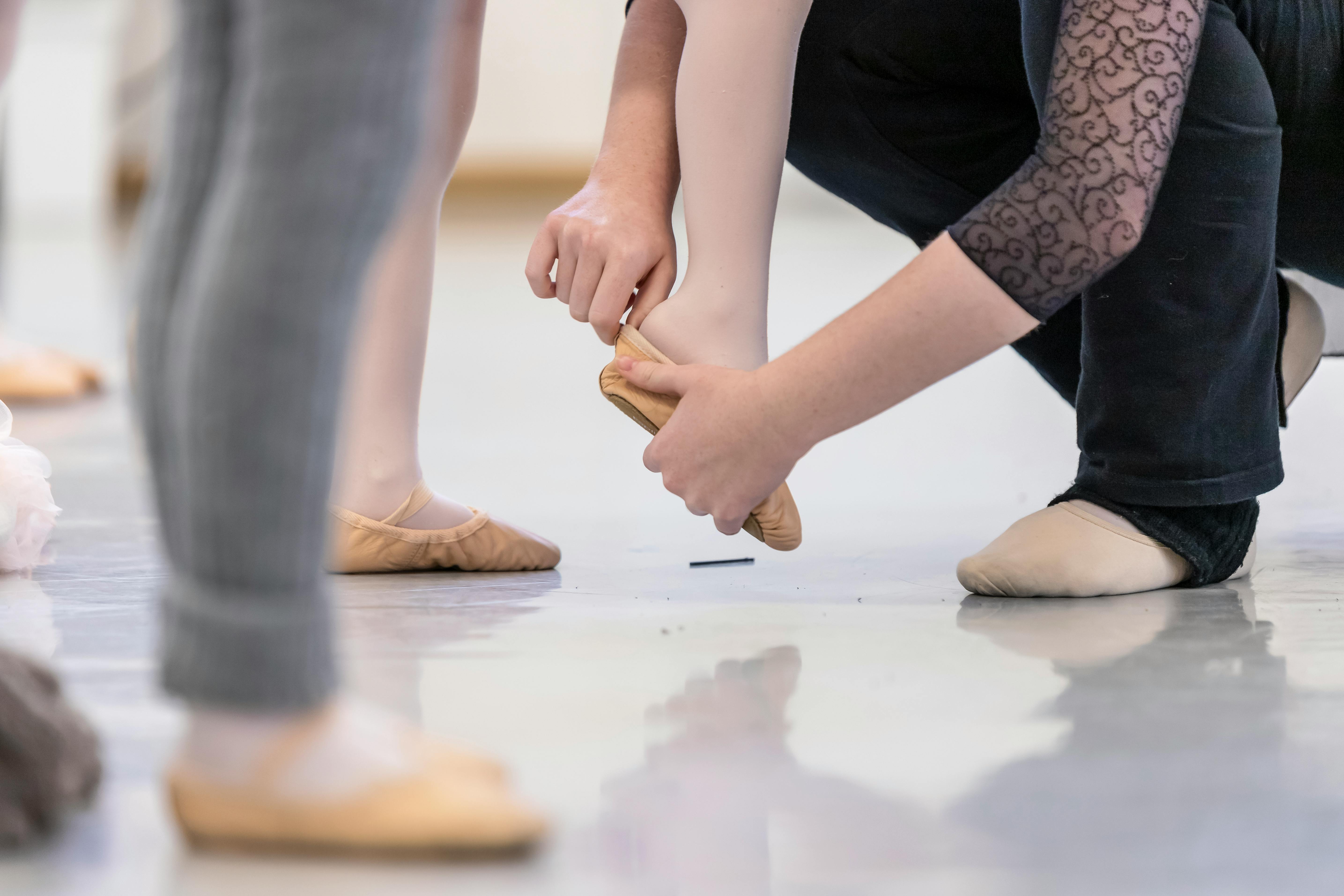 Dance teacher helping child put ballet shoes on